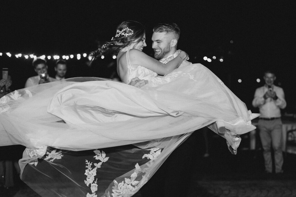 groom picks up bride and spins during bride and grooms first dance outdoors in the courtyard surrounded by twinkle lights at Rome countryside wedding held at Tenuta La Porta Sul Lago photographed by Destination Wedding Photographer Brittany Navin Photography