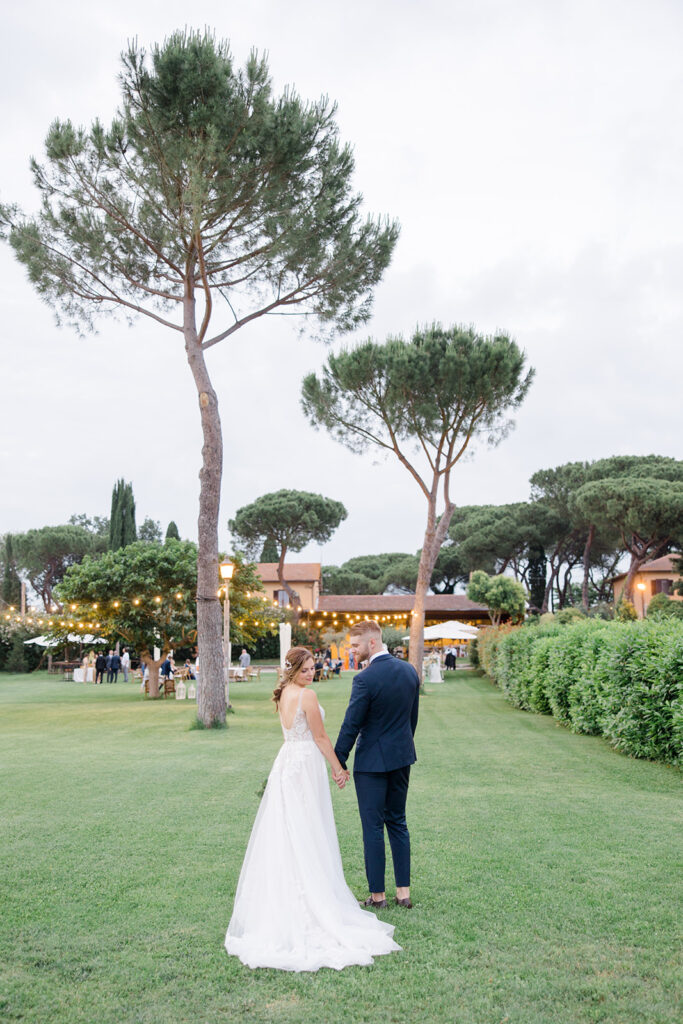bride and groom walking towards their recption space with centenary pines at Rome countryside wedding held at Tenuta La Porta Sul Lago photographed by Destination Wedding Photographer Brittany Navin Photography