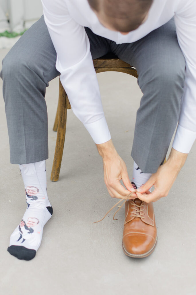 groom putting on shoes showcasing his customized socks with him and his brides faces all over them at Bleeks and Bergamot wedding in Ashton, Ontario photographed by Ottawa wedding photographer, Brittany Navin Photography
