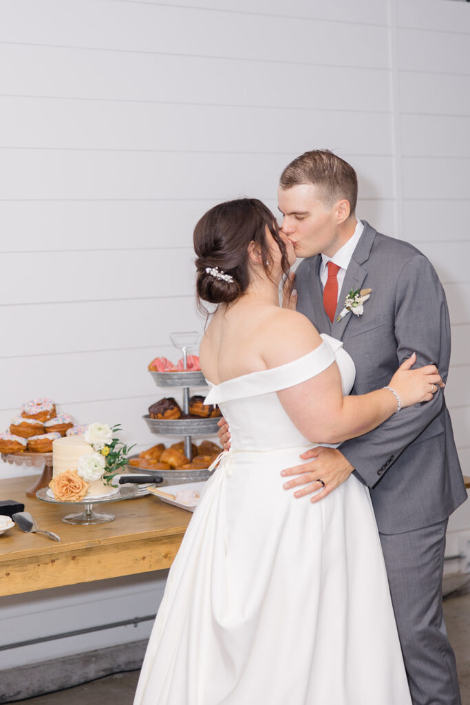 bride and groom share a kiss after cutting their cake at Bleeks and Bergamot wedding in Ashton, Ontario photographed by Ottawa wedding photographer, Brittany Navin Photography
