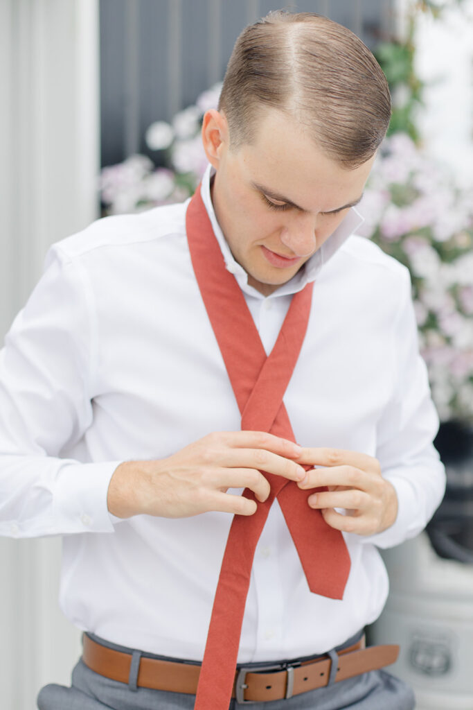 groom tying his teracotta coloured tie the morning of the wedding at Bleeks and Bergamot wedding in Ashton, Ontario photographed by Ottawa wedding photographer, Brittany Navin Photography