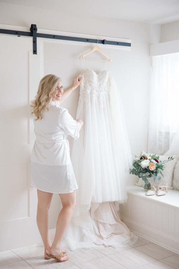 bride reaching for her dress hung up in the farmhouse bridal suite at Stonefields Estate wedding photographed by Ottawa Wedding Photographer Brittany Navin Photography