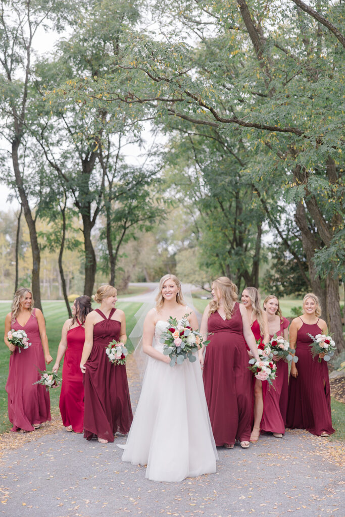 bride and bridesmaids walking together, bridesmaids are wearing a burgundy and rose colour palette at Stonefields Estate wedding photographed by Ottawa Wedding Photographer Brittany Navin Photography