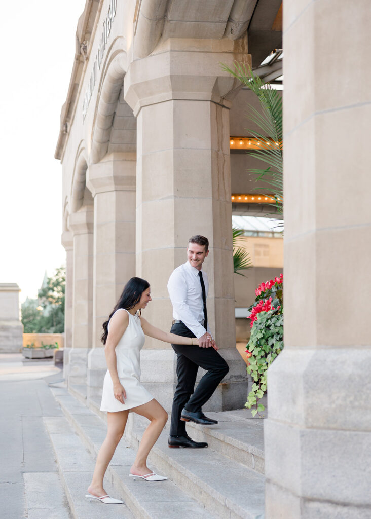Couple walking up the steps during their Château Laurier engagement photos, wearing modern, classic white and black outfits.
