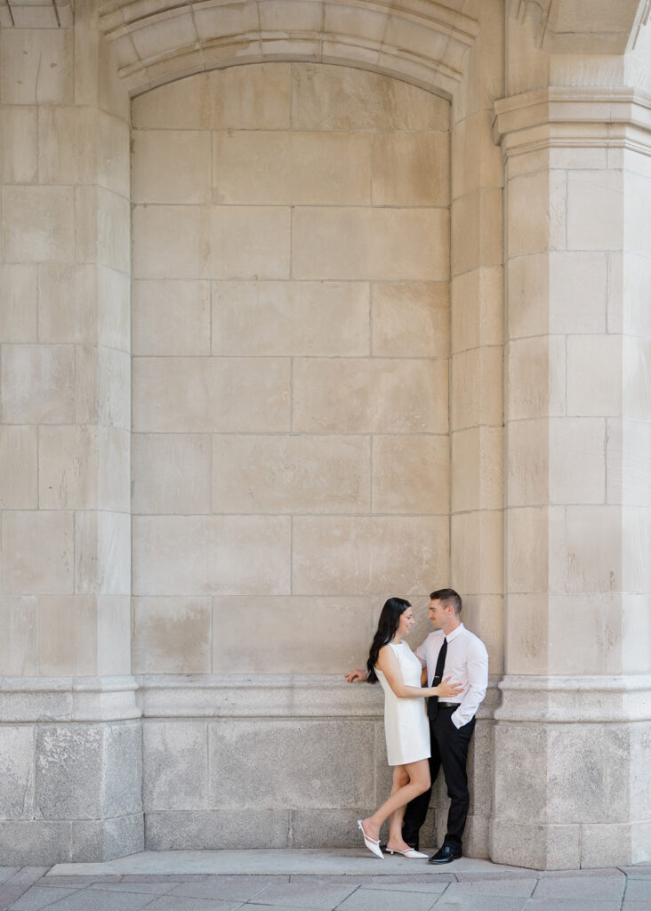 Engaged couple standing together under the grand stone archway at the Château Laurier during their summer engagement session in Ottawa.