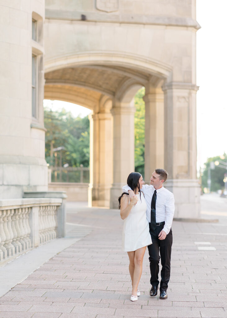 Engaged couple standing together under the grand stone archway at the Château Laurier during their summer engagement session in Ottawa.