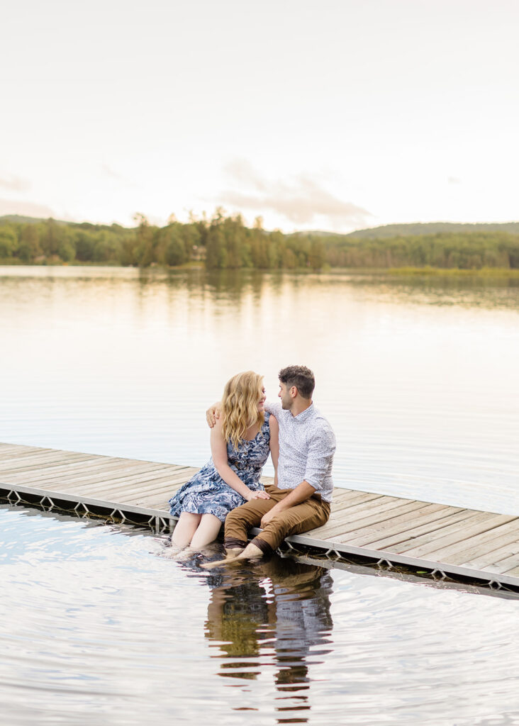 Couple sitting side by side on the dock with their feet in the water at waterfront private property engagement session 