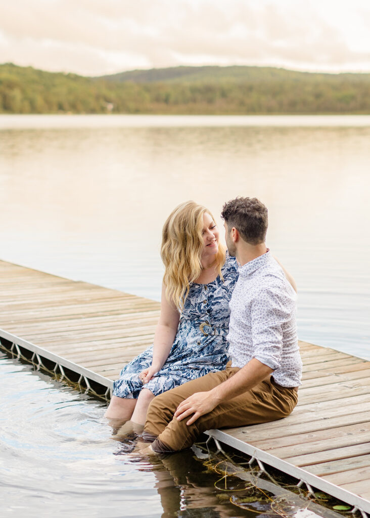 Couple sitting side by side on the dock with their feet in the water at waterfront private property engagement session 