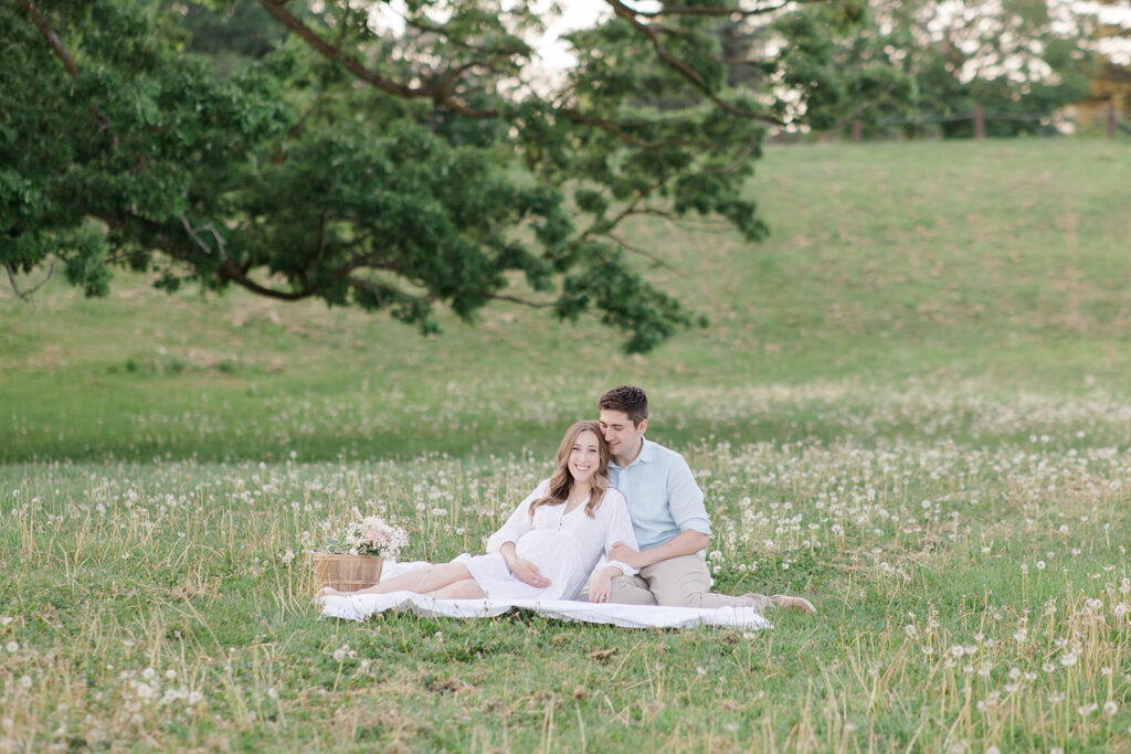 couple cuddling on picnic blanket in field at dominion arboretum maternity session in Ottawa photographed by Brittany Navin