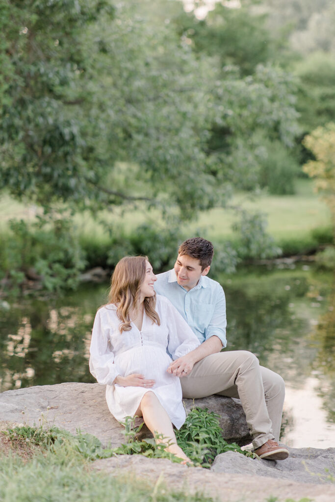 couple sitting on rocks together by the water at dominion arboretum maternity session in Ottawa photographed by Brittany Navin